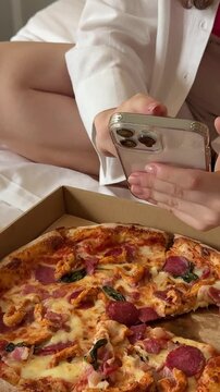 eating pizza in bed with a mobile phone teen girl listening to music on smartphone sitting in fast food cafe. baby girl eating pizza