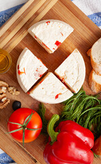 Top view on cut cheese heads on wooden board served with tomatoes, bell pepper and fresh herbs, olive oil, olives and bread. Serving French homemade cheese. Food concept