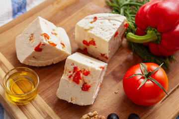 Variety of home made cheese and paprica and herbs, olive oil, olives and bread on a wooden board. Brined curd white cheese with vegetables on the table