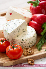 Cut cheese heads on wooden board served with tomatoes and fresh paprica and herbs, olive oil, olives and bread. Serving French homemade cheese. Food concept