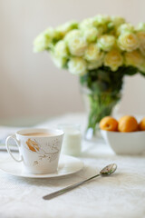 A cup of delicious morning coffee with organic yogurt, apricots and a bouquet of cream roses in the background. Selective soft focus