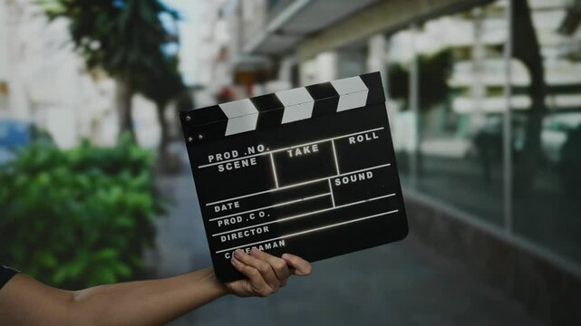 Man holding clapperboard on city street for film production, showcasing filmmaking process in urban setting, reflecting vibrant outdoor atmosphere.