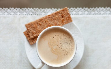 Top view of a tablecloth covered with a cup of delicious morning coffee and slice of fitness bread.