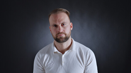 A man in a white shirt stands confidently, his serious expression and direct gaze conveying...