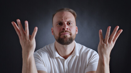 Man in white shirt raises hands, displaying confusion and disbelief. Close-up shot accentuates...