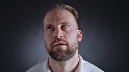 A man with a beard and blue eyes gazes upward, his expression reflecting curiosity and...