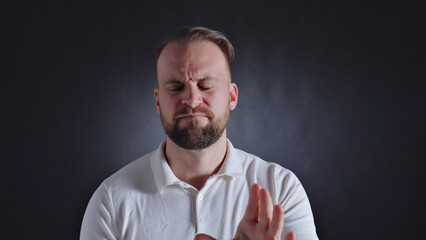Man in white shirt, eyes closed, frowning, hand gesture, dark background, possibly expressing frustration or disbelief.