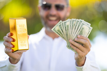 Business man holding a gold bar and cash. Gold financial success. Successful rich man holding gold and money. Business man with gold bars. Golden treasure and cash. Hands hold golden bars and cash.