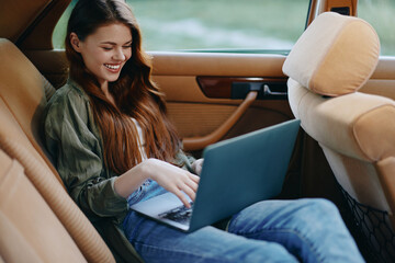 Young woman smiling while working on a laptop in a cozy car interior, wearing casual clothing and enjoying a productive day outdoors.