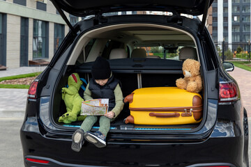 Cute little boy sitting in a car trunk before going on vacations with parents. Kid looking forward for a road trip or travel. Autumn break at school. Family travel by car.