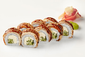 Delicious sushi rolls with eel, cucumber, cream cheese, sesame seeds, and unagi sauce on white background