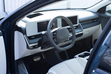 Steering wheel of a electric vehicle, interior cockpit, electric buttons, digital speedometer, front seats, textile, windows, console, gear shift. Car dashboard with a digital touchscreen