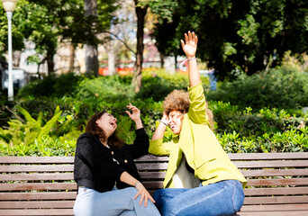 Naklejka premium Two businesswomen are sitting on a bench in a park, laughing and having fun