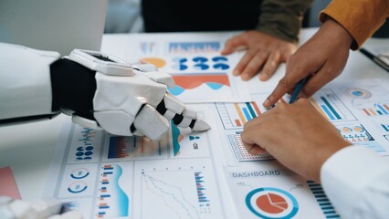 A robot hand and human hands engage in a collaborative analysis of various data charts and dashboards during a strategic business meeting.Noogenesis