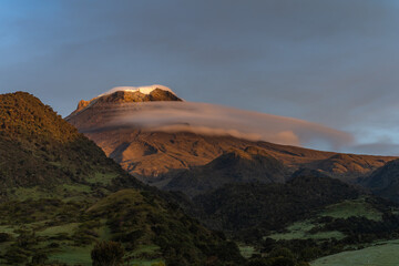View of snow-capped volcano at sunrise with a cloud under the ice on a Colombian farm, with natural colors in gold. Colombian Andes Nevado del Tolima