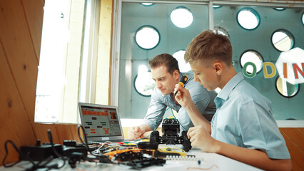 Caucasian teacher help student fixing car model and giving advise for programing system or coding...