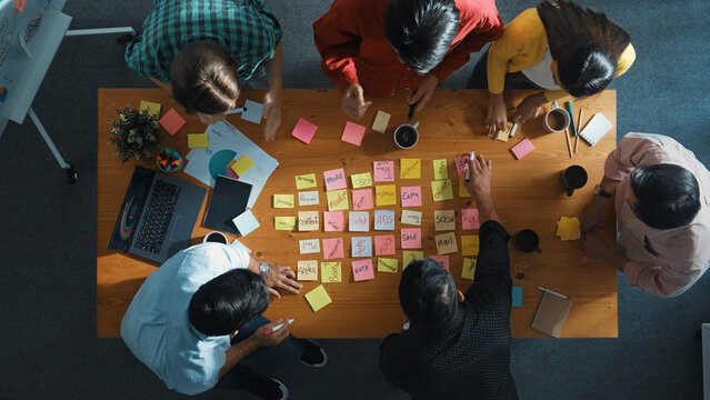 Top view of smart diverse business team working together and clapping hand while brainstorming marketing idea or creative startup project by using sticky notes and stick at meeting table. Convocation.