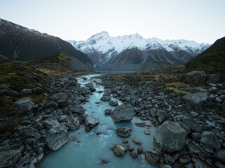 Alpine nature landscape of the Hooker Valley Track, snow covered Southern Alps mountains, green valley and turquoise glacier river in New Zealand