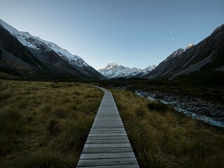 Wooden walkway boardwalk hiking trail path leading to alpine snow covered Southern Alps mountains, Hooker Valley Track, Aoraki Mount Cook New Zealand