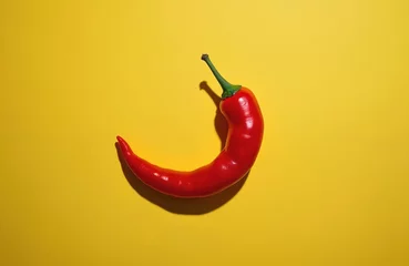 Vibrant red hot pepper on sunny yellow background. Fresh organic chili with green stem casting hard shadow. Culinary ingredient for spicy dishes, mexican cuisine, healthy eating concept. Minimalist