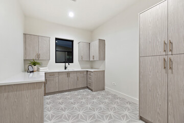 A laundry room that features numerous cabinets, a sink, and a window