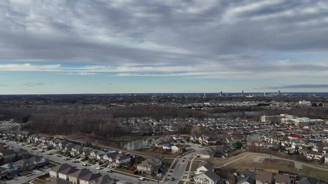 Drone ascending over a cityscape with leafless trees and small pond under overcast sky at sunset