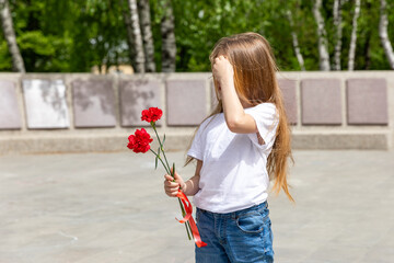 Victory Day. Little Girl with red carnations at the Eternal flame near the monument of Unknown soldiers tomb. Patriotic education at school.