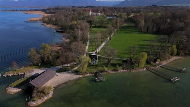 Drone view of Holy Cross Chapel on Herreninsel, Bavaria. Historic baroque chapel blends with alpine scenery, clear skies, tranquil lake and springtime nature. Luftaufnahme Seekapelle zum Hl. Kreuz. 