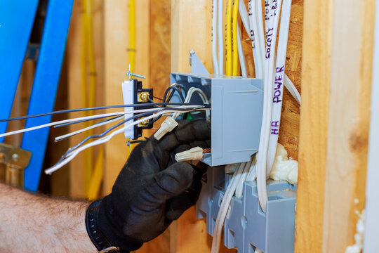 An electrician connects wires to junction box while installing electrical systems in new home.