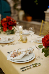 Knotted napkin lies on a plate on a set table next to a red bouquet of flowers