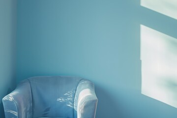 A light blue armchair sits in a room with blue walls. Sunlight casts a window shadow on the wall, A subtle gradient of light blue shades creating a soothing atmosphere
