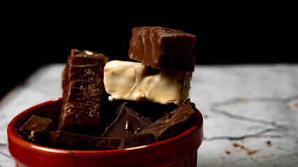 Assorted chocolate bars and chunks in red ceramic bowl on marble background