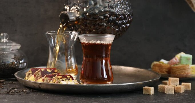Woman pouring hot Turkish tea into glass cup at black table, closeup