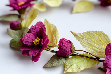 Close-up of magenta and pale yellow crepe paper flowers and leaves, arranged in a circular form on white background, suggesting springtime or floral decoration