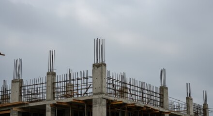 Building under construction showing concrete pillars and rebar against a cloudy sky.