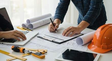 Architect or engineer working on blueprints with tools and laptop on desk.