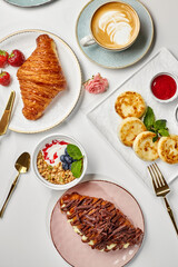 Delicious breakfast with croissants, pancakes, granola, cappuccino and berries served on white table
