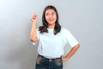 Cheerful young Asian woman with bright facial expression, smiling and pointing upward with one...