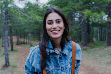Naklejka premium Portrait of a cheerful young woman enjoying a peaceful day in a lush pine forest, embracing the tranquility of nature