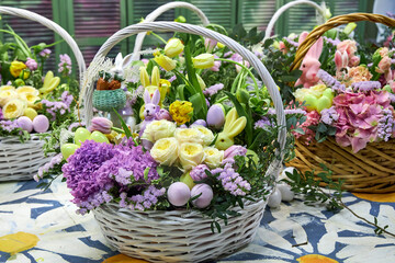 Close-up of large Easter baskets with live lilac and yellow flowers and bunnies standing on the...