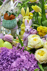 Close-up of large Easter baskets with live lilac and yellow flowers and bunnies standing on the table