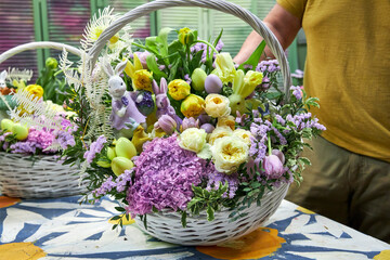 Close-up of a male florist in a yellow T-shirt holding a large Easter basket with lilac and yellow...