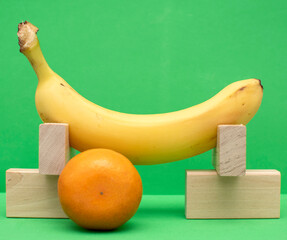 Still life with wooden blocks, tangerine and banana on a green background	