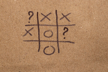 Children's game tic-tac-toe and question marks drawn on brown paper with black marker, tic-tac-toe