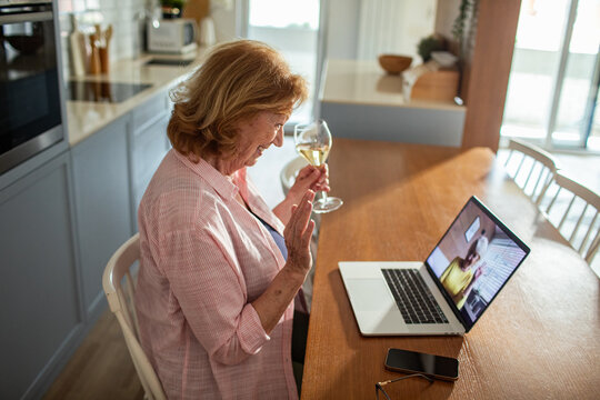 Senior woman video calling with wine glass in hand enjoying virtual date on laptop