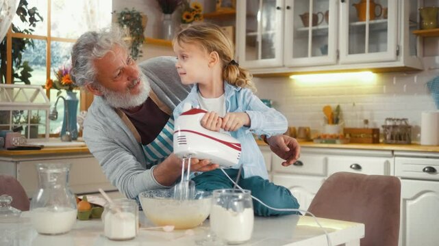 Smiling Little boy of 5 years using mixer machine to make pancake batter with his grandfather in the kitchen.