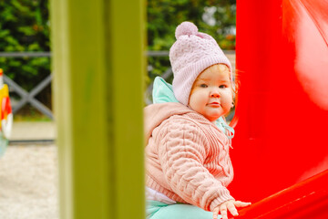 A young child wearing a knitted hat and cozy sweater explores a vibrant playground The setting features bright colors and a cheerful atmosphere perfect for outdoor fun