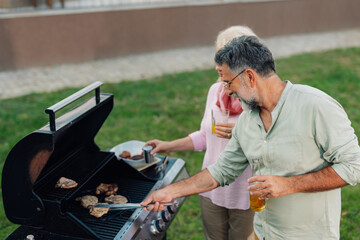 Senior couple grilling meat and enjoying drinks in backyard