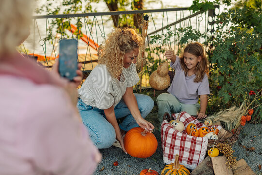 Family decorating pumpkins and gourds for autumn celebration in garden - Powered by Adobe