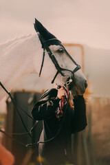 Portrait of a white horse being held by a young girl on a lead rope on a sunny day. The picture conveys the spirit of equestrian sports and the love for horses.